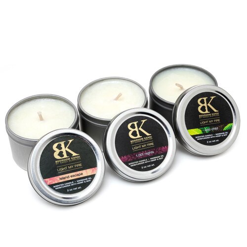 An image of three small massage oil candle tins in a row with their lids propped up in front of them, displaying the fragrances.